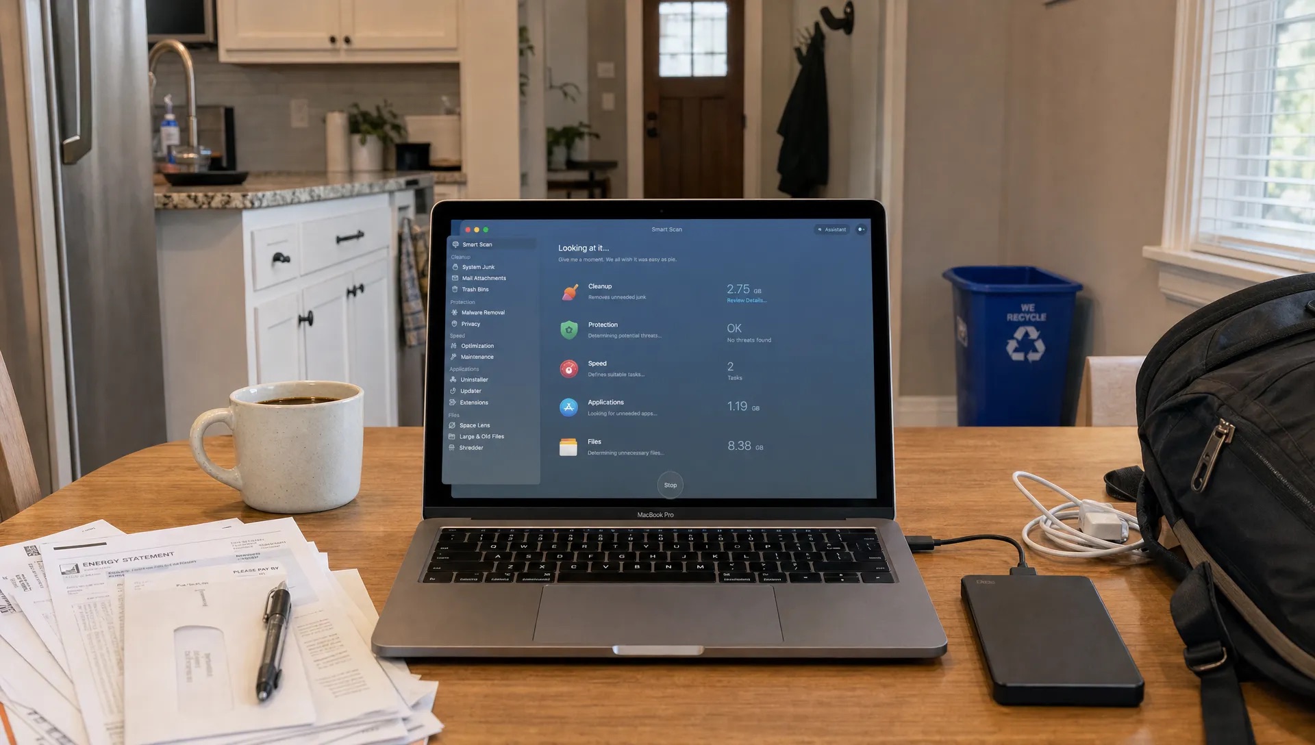 A MacBook on a kitchen table shows a cleanup app beside everyday items and a small recycling bin.