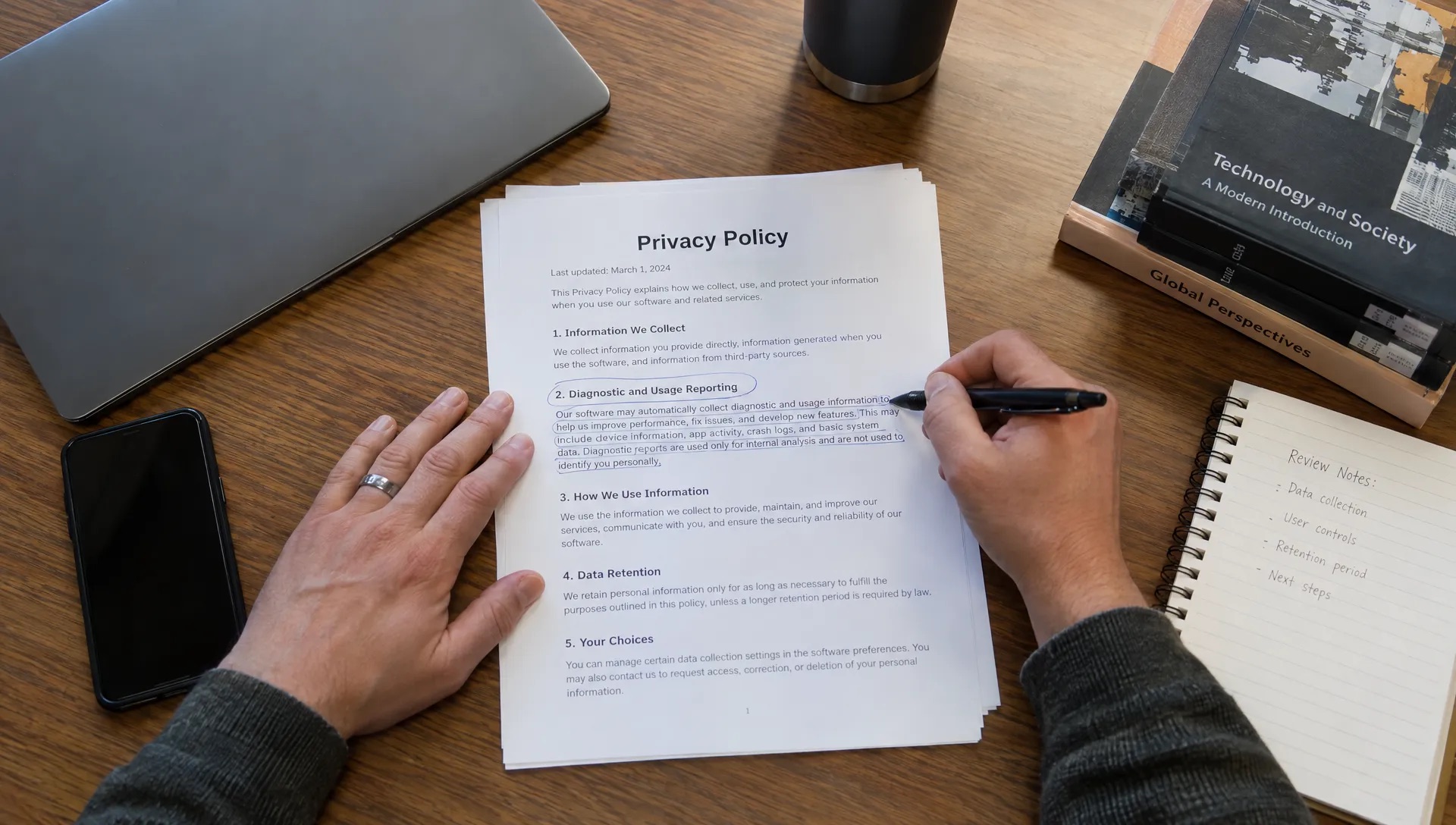 Hands mark a software privacy policy beside a closed laptop while checking what diagnostic information an app may collect.