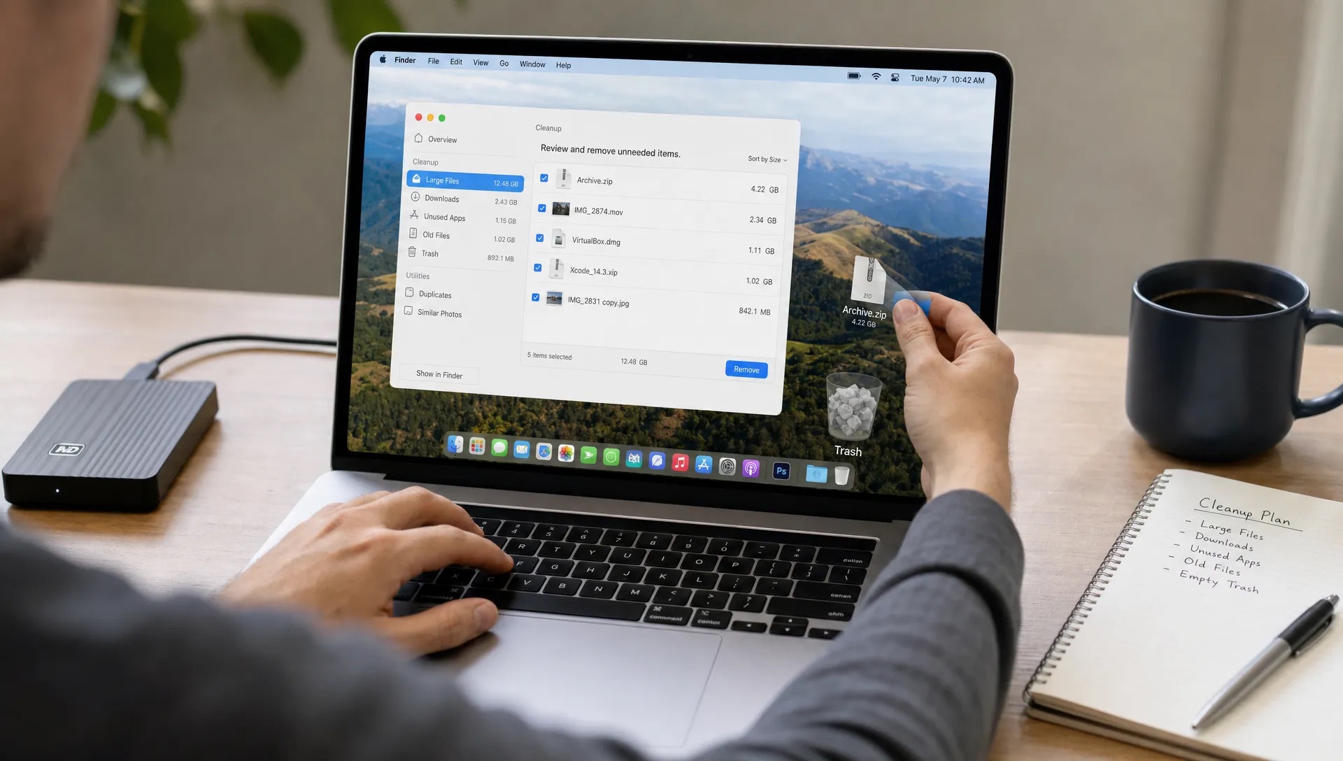 Hands use a MacBook to move selected files toward the Trash during a cleanup session.